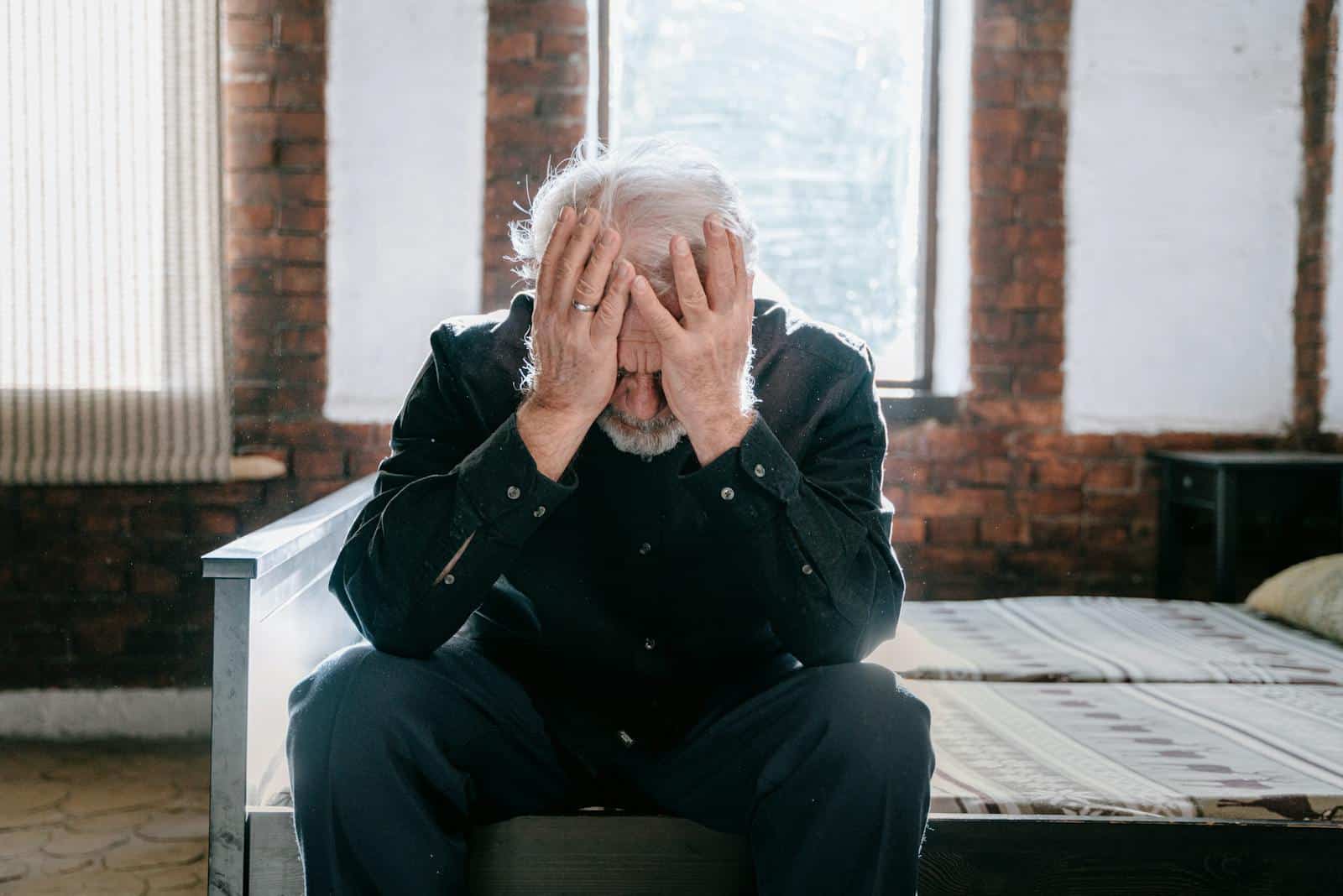 An elderly man sitting on a bed indoors, expressing grief and loss because he didn't break free from golden handcuffs